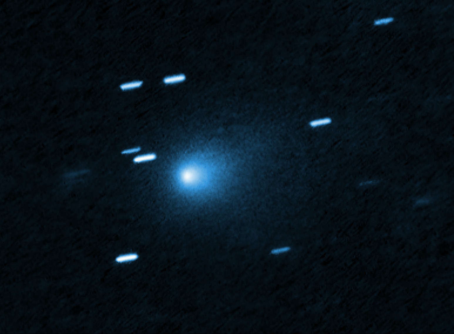 Hubble Space Telescope image of interstellar comet 3I/ATLAS showing a bright blue core and a faint dust halo, with streaked background stars.