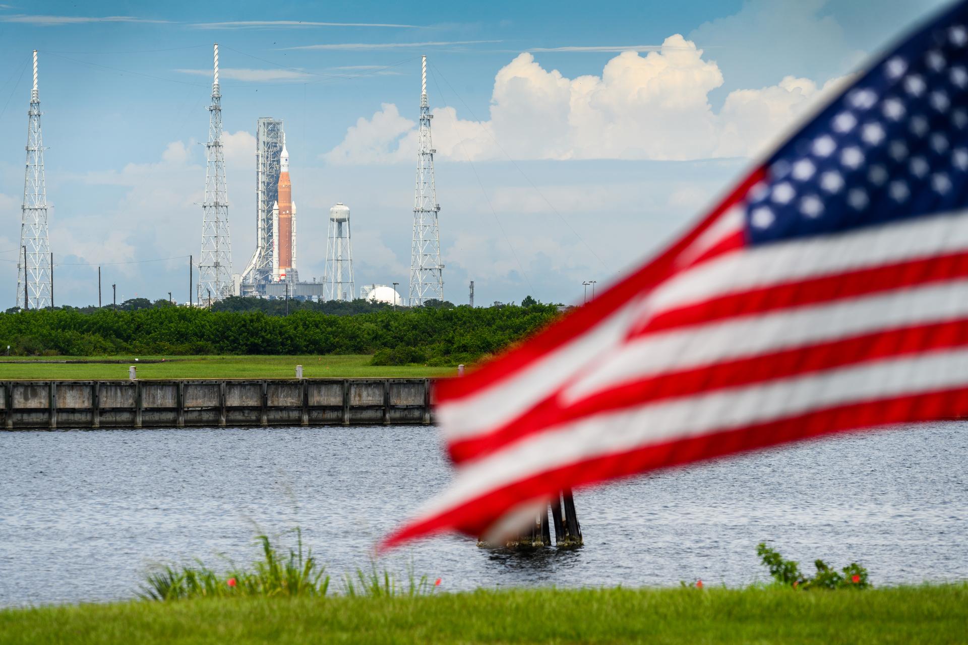 NASA’s SLS rocket on the launch pad at Kennedy Space Center with the U.S. flag in the foreground.